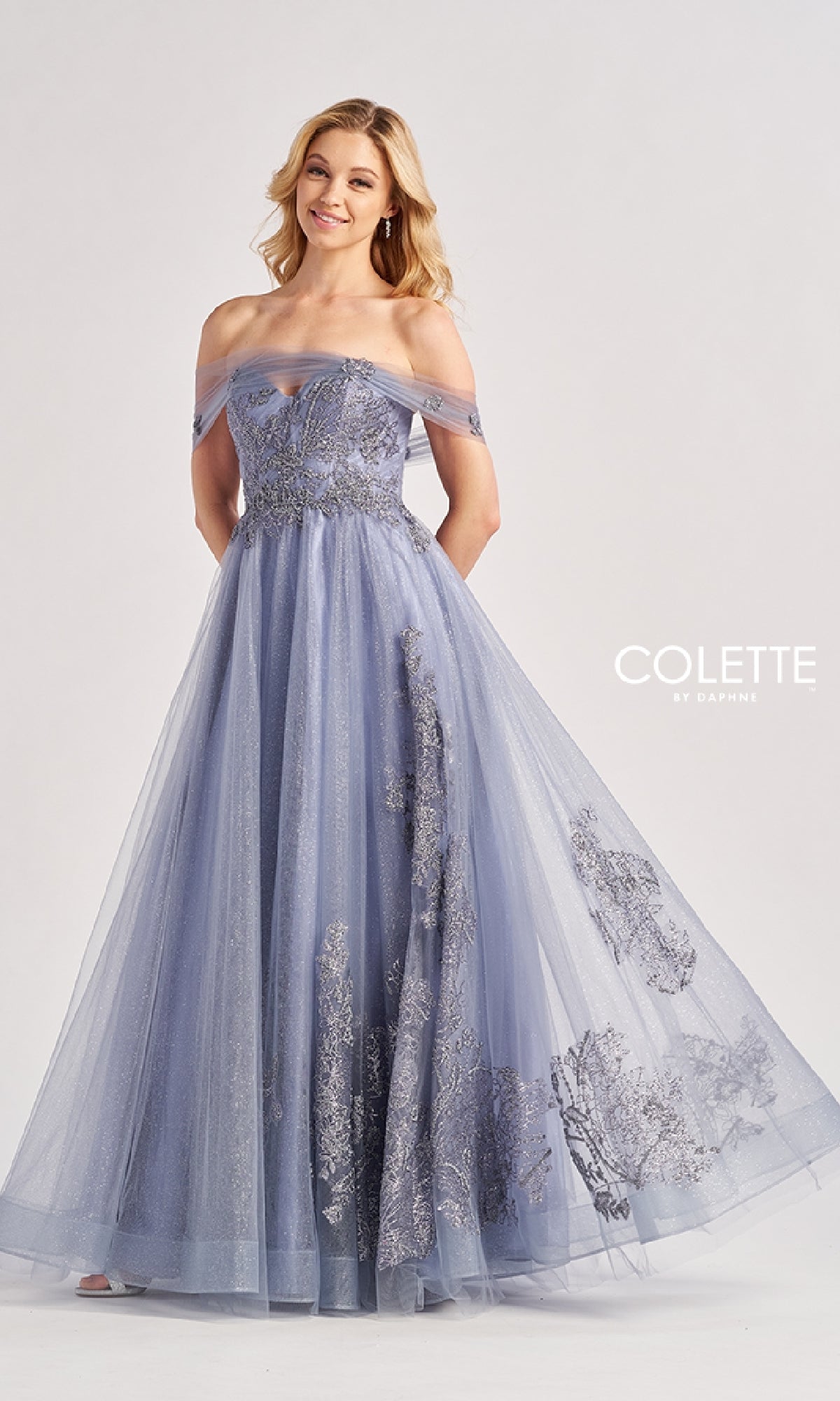 A woman in the Colette by Daphne Long Prom Dress CL8640, featuring a floor-length, sweetheart neckline in lavender with silver floral embroidery, stands against a plain background. The
